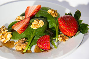 spinach, strawberries, walnuts, and dressing on a white plate